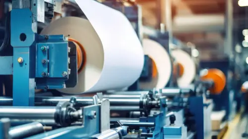 A close-up of an industrial machine processing a continuous white sheet through rollers in a manufacturing line